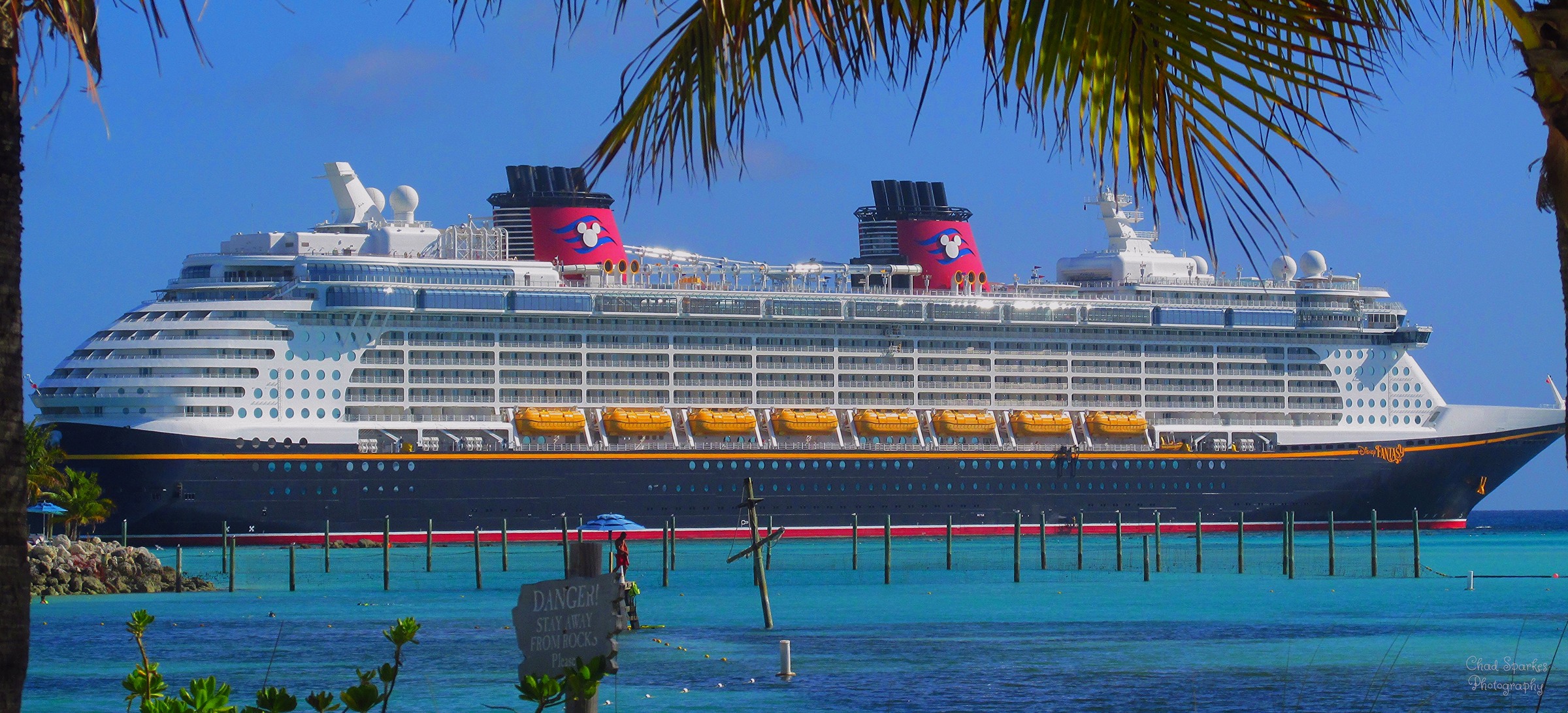 Disney Fantasy docked at Disney Castaway Cay behind palm trees