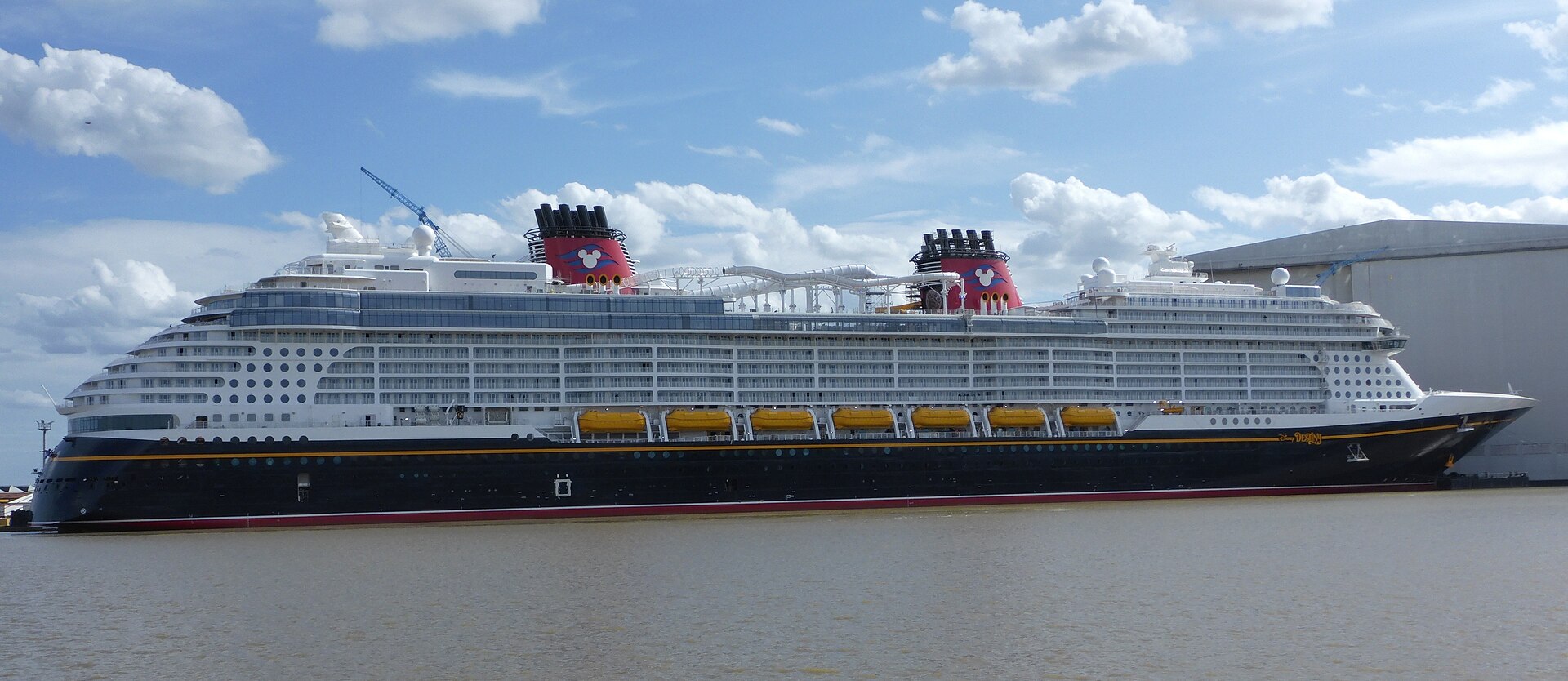 Disney Destiny shown broadside with its navy hull, white decks and red funnels